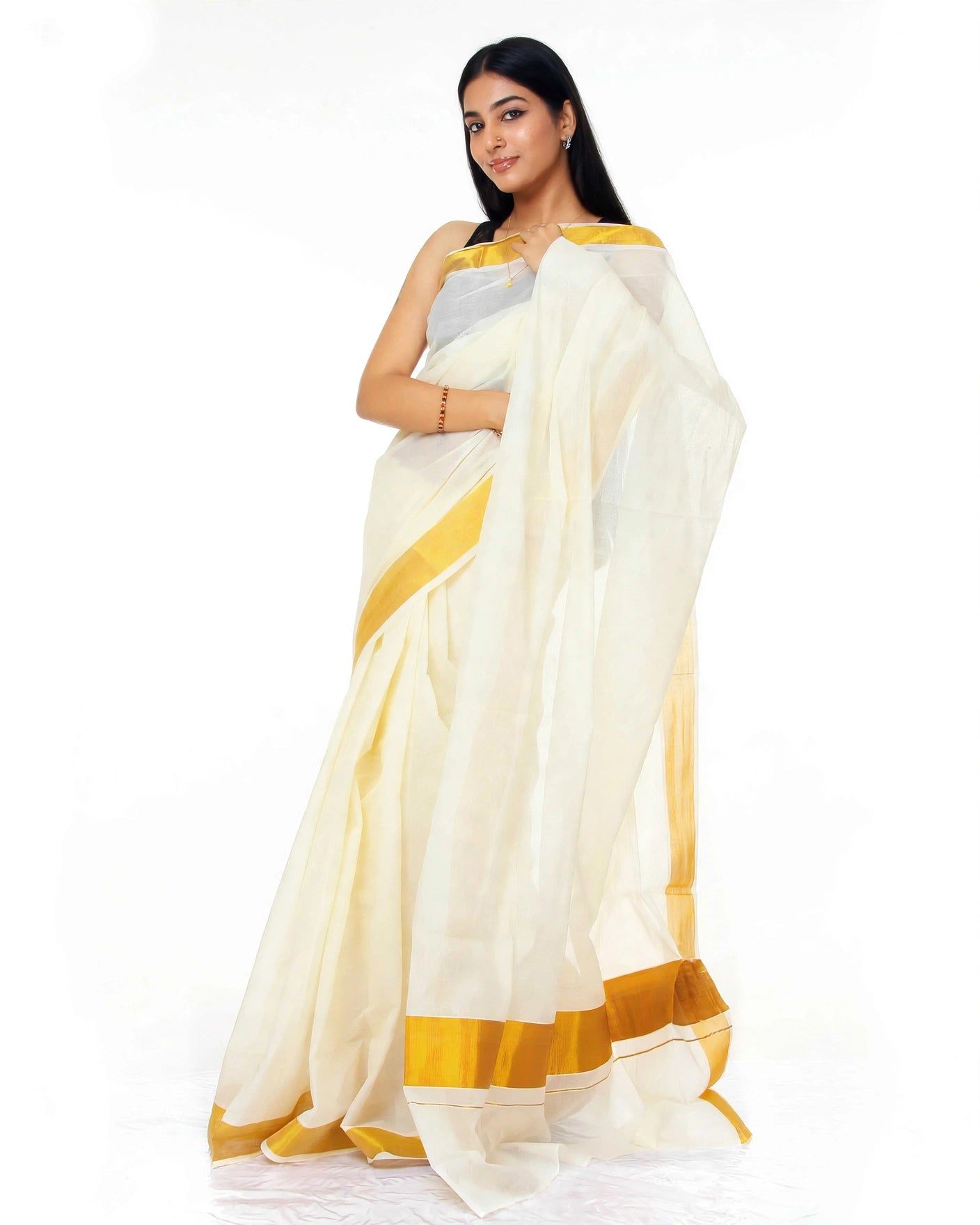 A woman modeling a white saree with mustard yellow borders and a silver blouse against a plain white background.