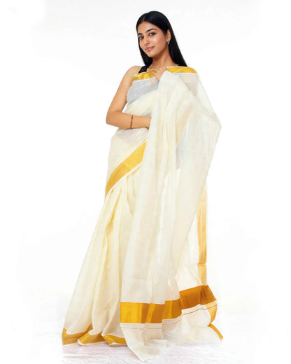 A woman modeling a white saree with mustard yellow borders and a silver blouse against a plain white background.